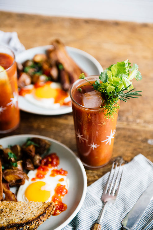Load image into Gallery viewer, a homemade bloody mary with fresh garnishes next to a breakfast plate of potatoes, eggs, toast and bacon
