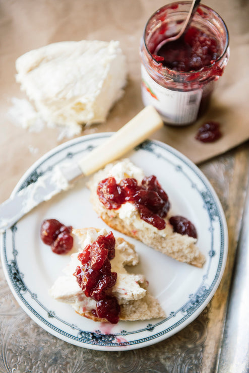 Load image into Gallery viewer, Plate with bread topped with cheese and jam, jar of jam, and knife on a wooden surface.