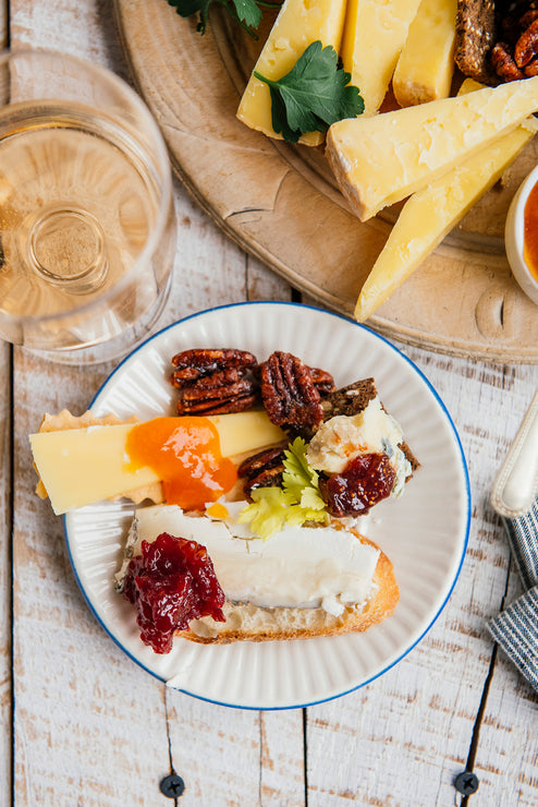 Load image into Gallery viewer, Plated appetizer with cheese, preserves, and crackers on a wooden table with a glass of white wine.