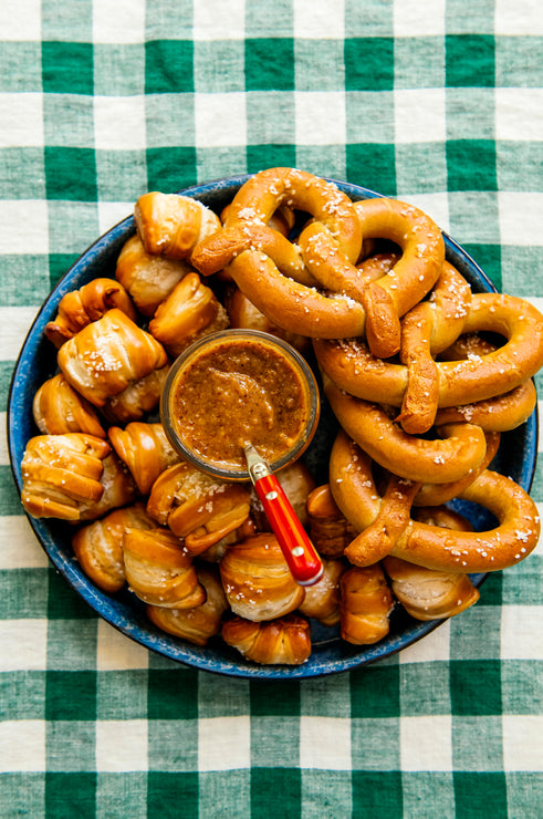 Load image into Gallery viewer, A blue circular tray with soft pretzels and golden ale mustard, set on a green and white checked tablecloth.