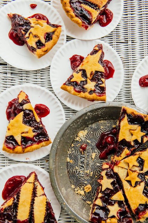 Load image into Gallery viewer, Slices of cherry pie with crust stars on white plates on a white rattan table.