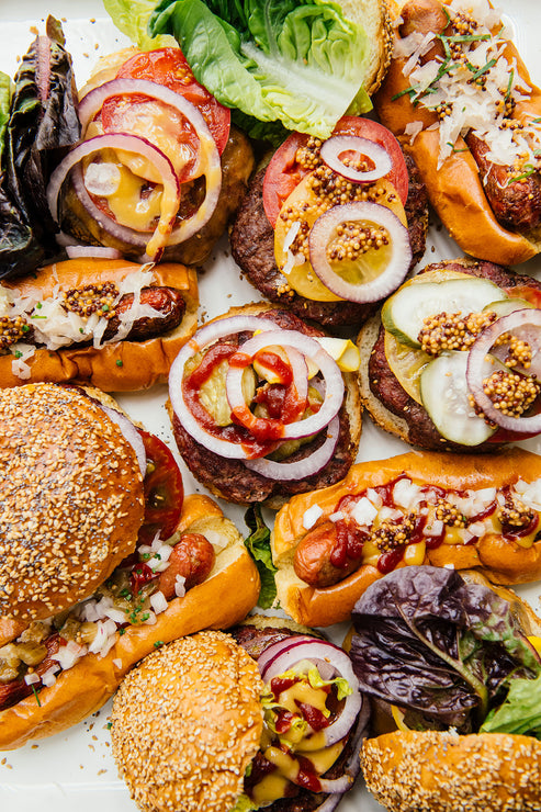 Load image into Gallery viewer, a platter of hamburgers and hot dogs with a variety of toppings