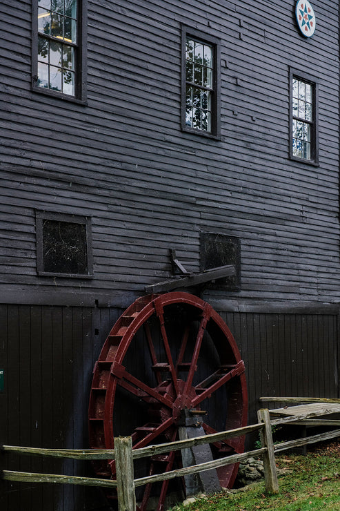 Load image into Gallery viewer, Red water wheel attached to a wooden building with windows.