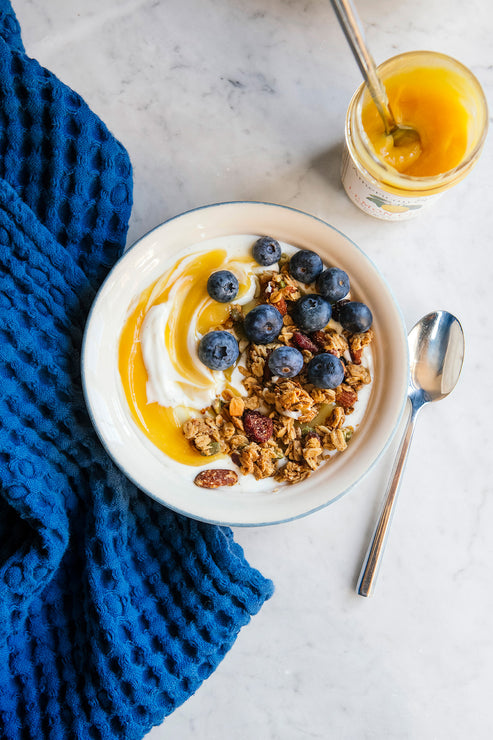 Load image into Gallery viewer, A bowl of yogurt topped with lemon curd, blueberries and maple granola next to an open jar of Lemon Curd and a blue tea towel