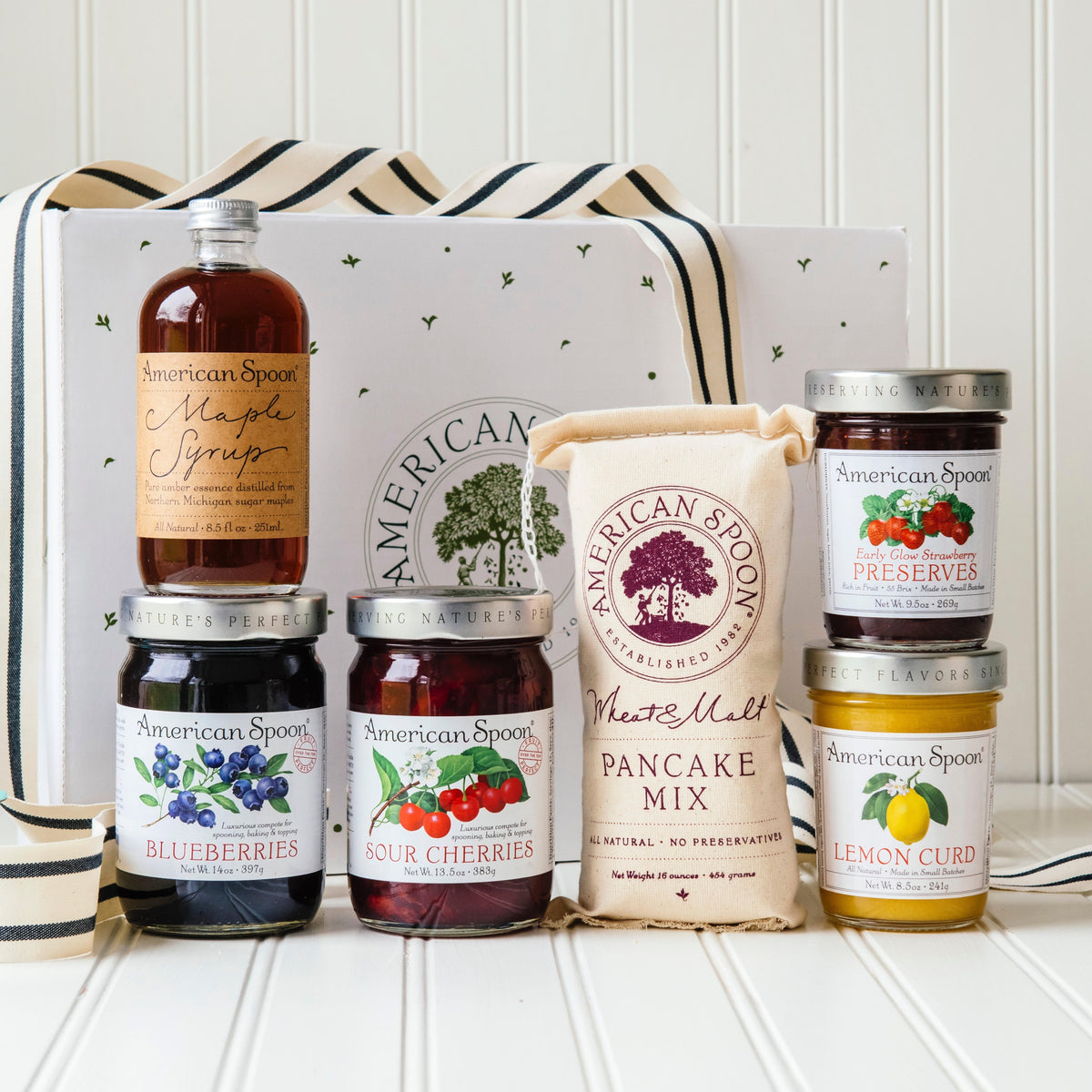 Up North Breakfast gift box showing Maple Syrup, Fruit Perfect Blueberries, Fruit Perfect Sour Cherries, Wheat & Malt Pancake Mix, Early Glow Strawberry Preserves, Lemon Curd a gift box and ribbon. 