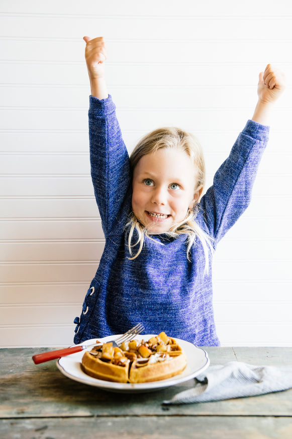a young girl giving thumbs up to a plate of homemade waffles