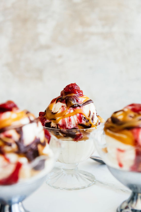 Ice cream sundaes topped with cherries, caramel and fudge sauce in glass dishes