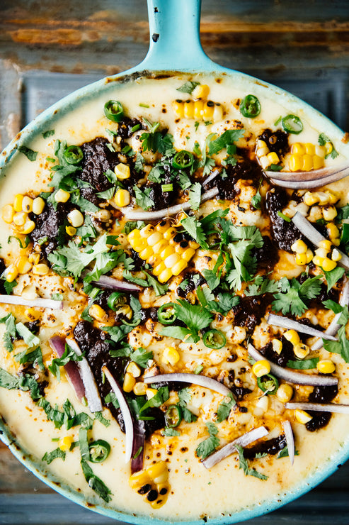 Load image into Gallery viewer, A skillet of melty queso dip topped with sweet corn, slivers of red onion, cilantro, and Dried Chile Salsa
