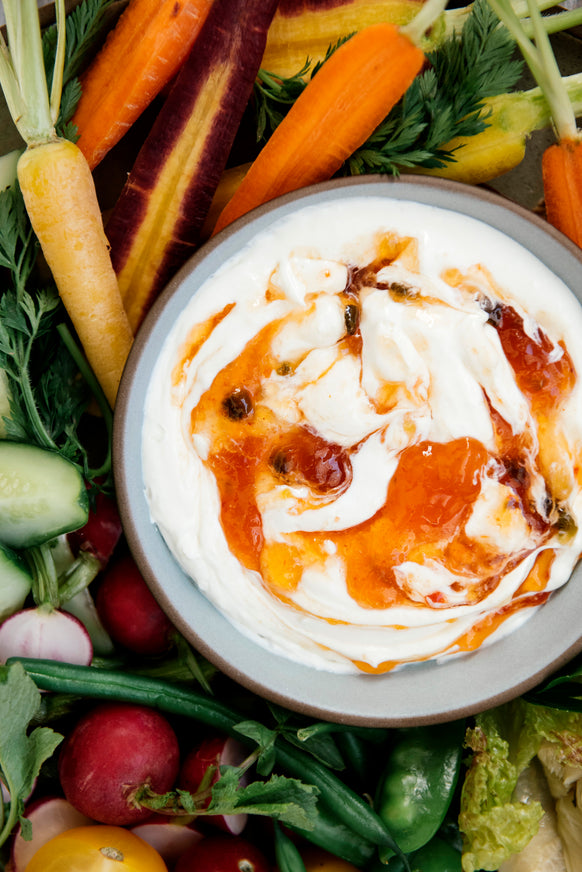 a tray of freshly cut vegetables with a dip topped with pepper jelly