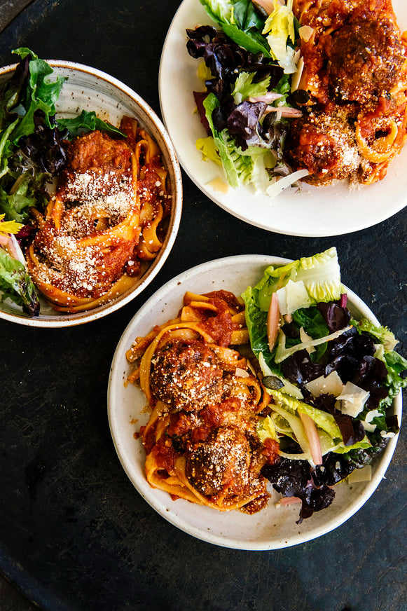 plates of spaghetti and meatballs with a side salad