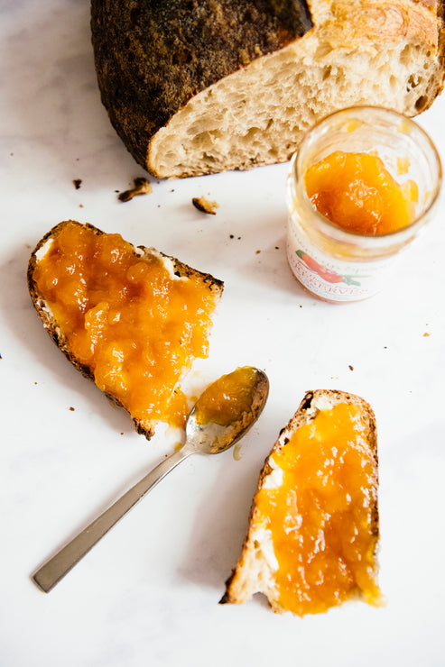 Load image into Gallery viewer, A piece of toast topped with Leelanau Apricot Preserves next to a loaf of bread
