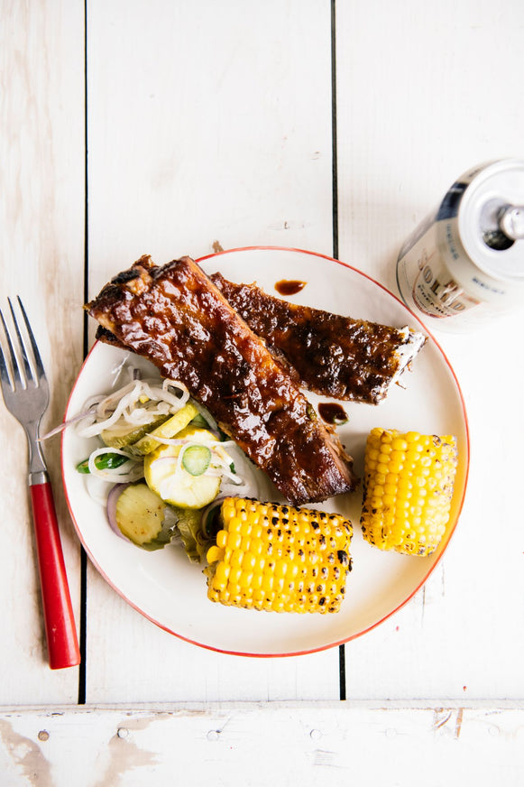 a plate of ribs, pickles, slaw and corn