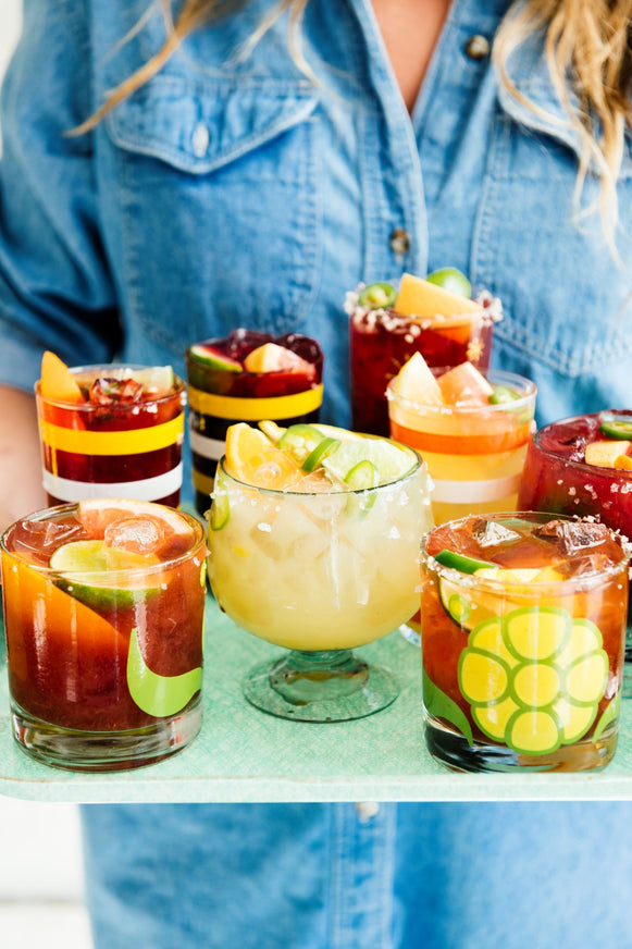 a tray filled with glasses of homemade cocktails with fresh fruit garnishes
