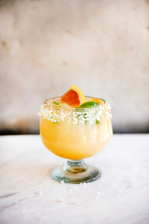 Load image into Gallery viewer, Margarita cocktail in a glass with salted rim and fresh citrus on a marble surface
