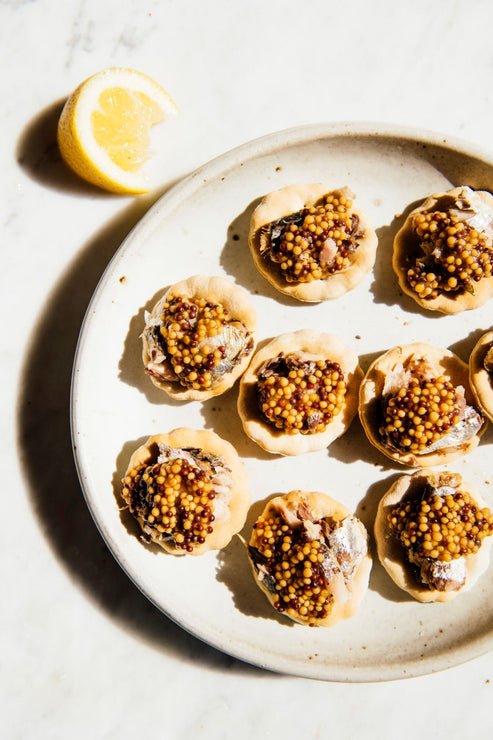 Load image into Gallery viewer, a plate of crackers topped with sardines and whole seed mustard with a wedge of lemon
