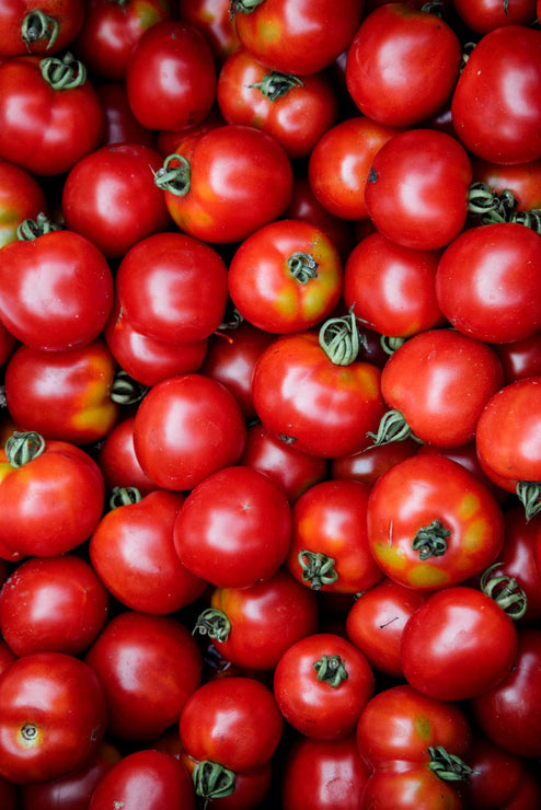 Load image into Gallery viewer, Close-up of a pile of red tomatoes with green stems.
