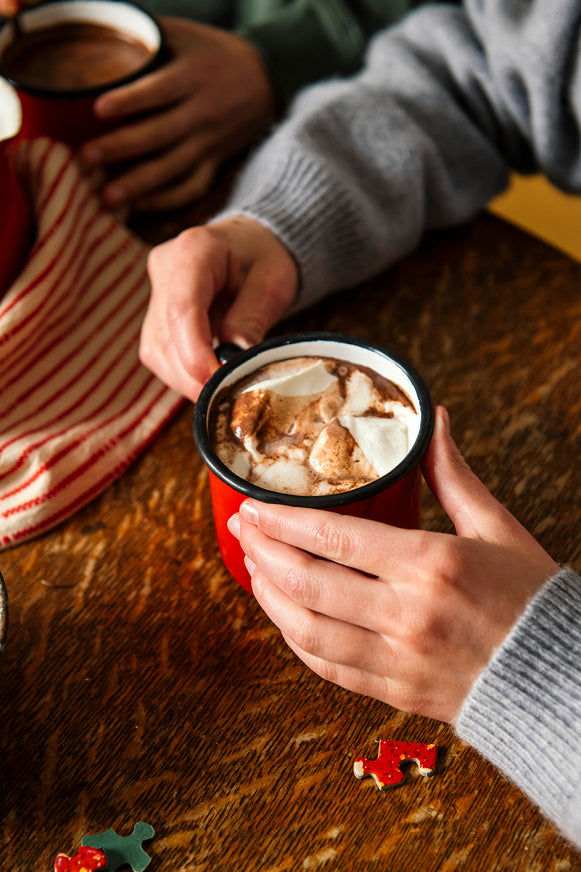Person holding a mug of hot chocolate with marshmallows on a wooden table.