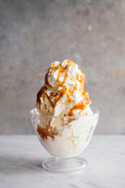 Load image into Gallery viewer, Ice cream with caramel drizzle in a glass bowl on a marble surface.
