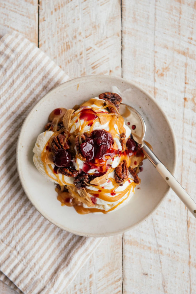 Ice cream sundae with fruit perfect cherries, candied pecans & caramel in a bowl with a spoon