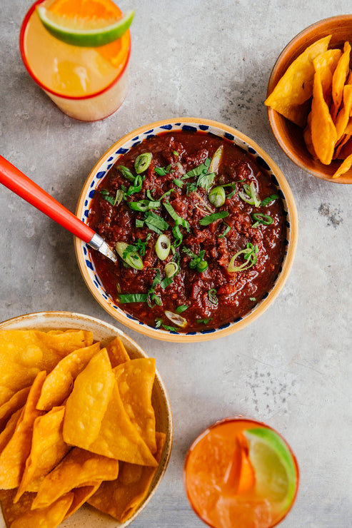 Load image into Gallery viewer, Bowl of Cherry Chipotle Salsa sprinkled with green onions next to bowls of tortilla chips and glasses of margaritas.
