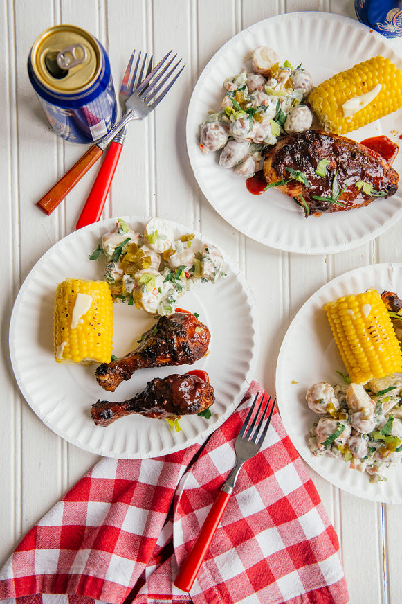 plates of bbq chicken drumsticks and thighs next to corn and potato salad