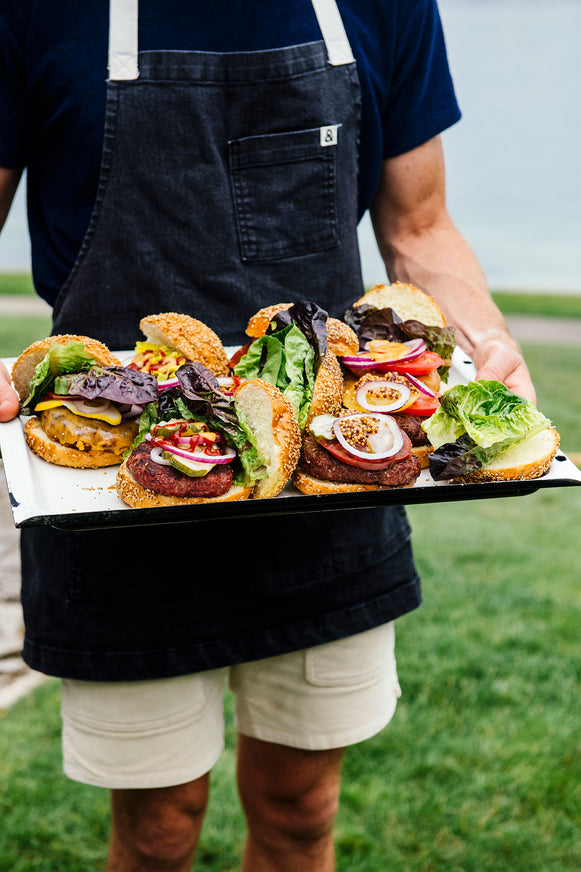 a man in an apron holding a platter of hamburgers