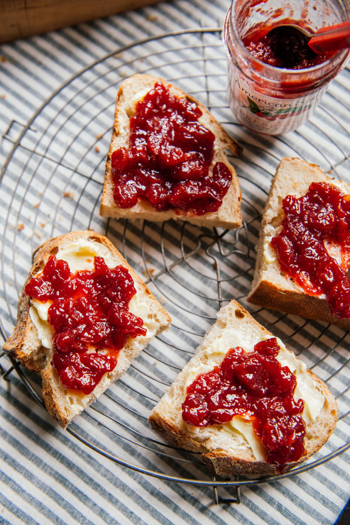 Load image into Gallery viewer, Three slices of bread with butter and sour chery preserves on a cooling rack, with a jar of preserves in the background.
