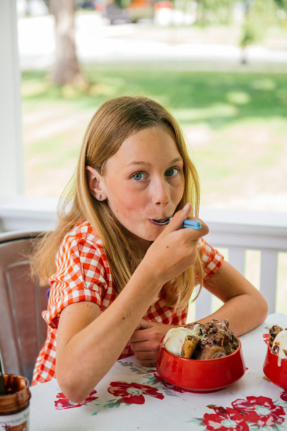 Young girl eating an ice cream sundae at a table with a floral tablecloth.