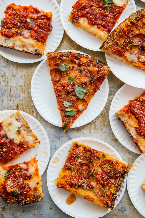 Load image into Gallery viewer, Multiple slices of pizza on paper plates arranged on a wooden table.
