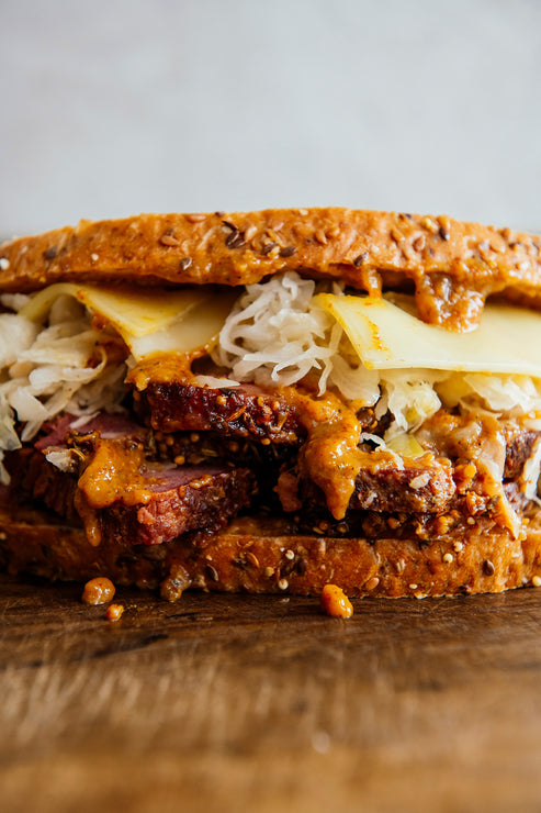 Load image into Gallery viewer, A giant pastrami sandwich with swiss cheese, sauerkraut, and Golden Ale Mustard on caraway rye.
