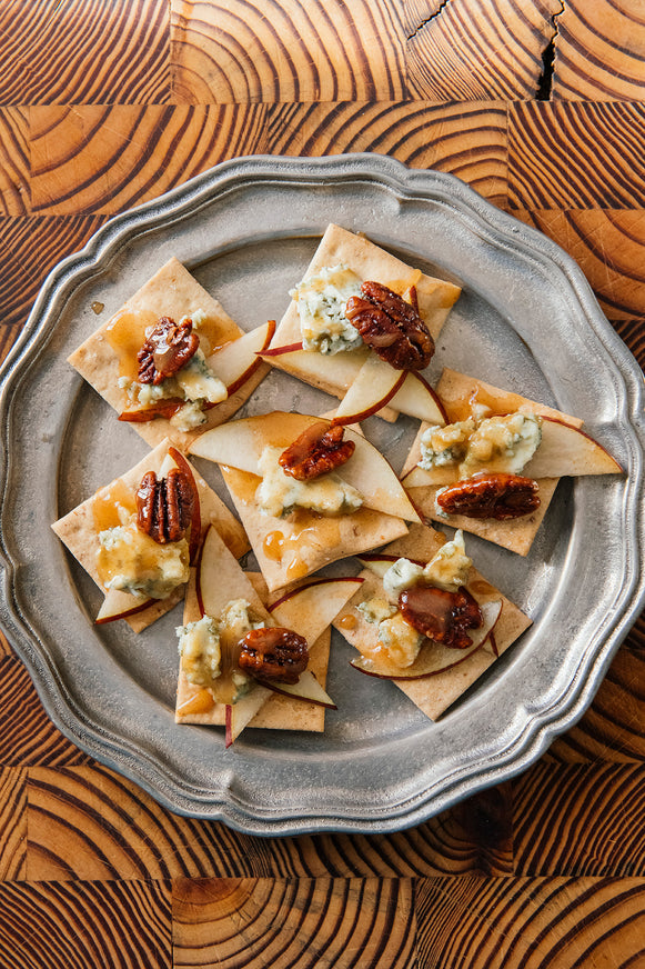 Silver platter of crackers topped with blue cheese, apples, and Candied Pecans on a wooden surface