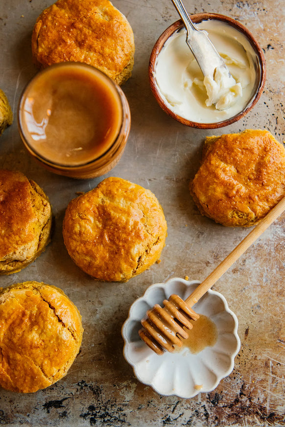 Pumpkin biscuits with small bowl of butter, open jar of honey and honey dipper resting on tiny plate.