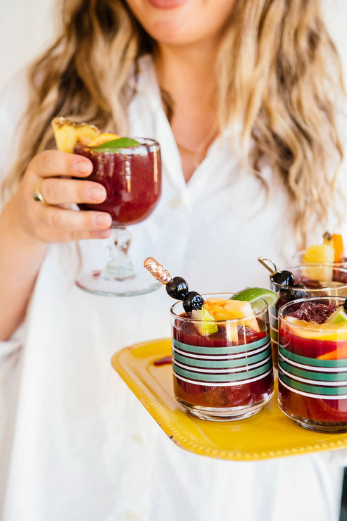 Load image into Gallery viewer, a woman holding a tray of cherry margaritas with fresh fruit garnishes
