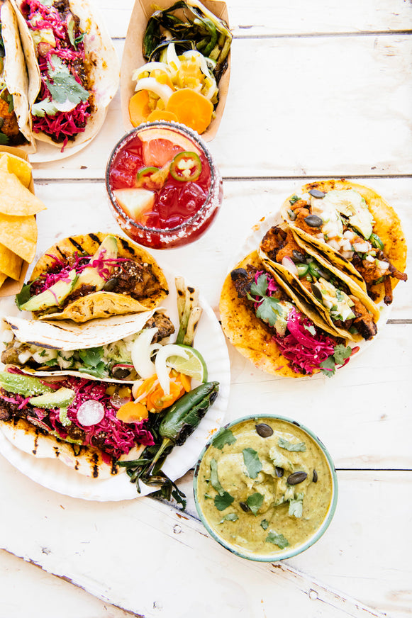 Plates of tacos topped with American Spoon salsa, a cocktail made with Paloma Mix and fresh guacamole
